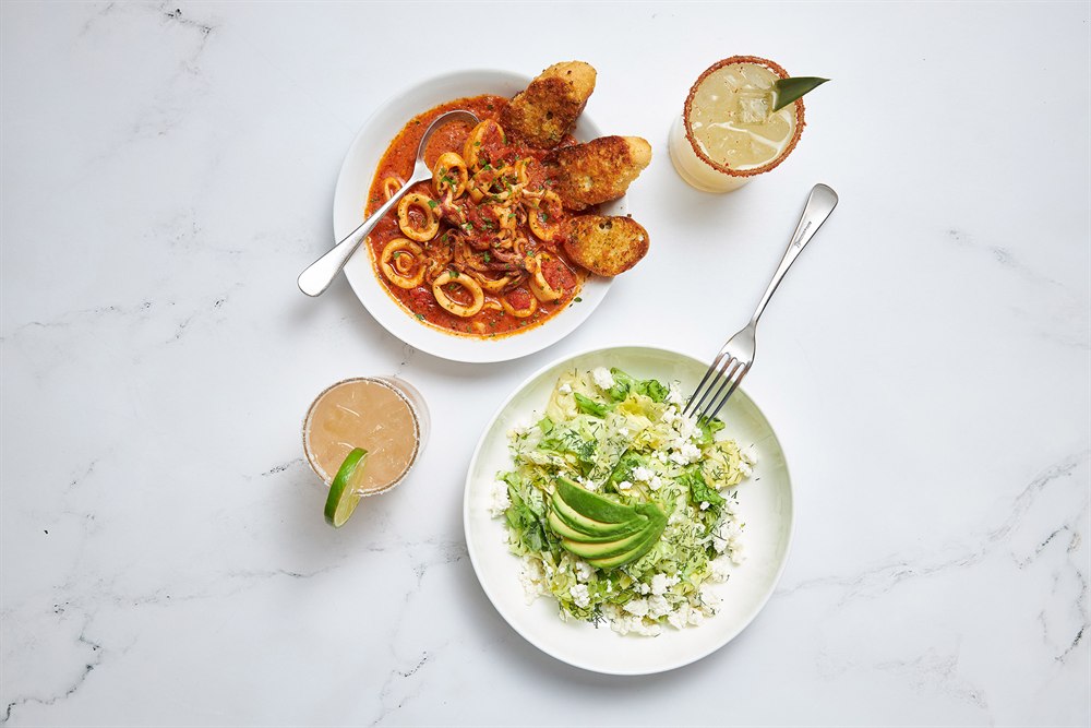 Overhead food photography: sauteed calamari, avocado salad and margaritas on marble, San Diego