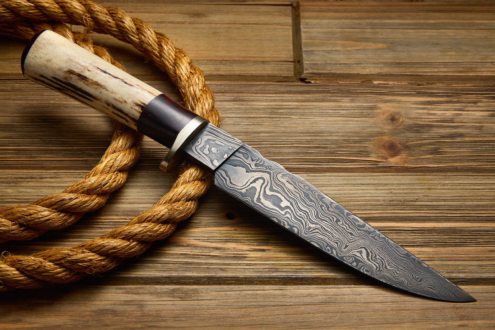 Custom damascus knife photographed on rustic wood with rope, front side