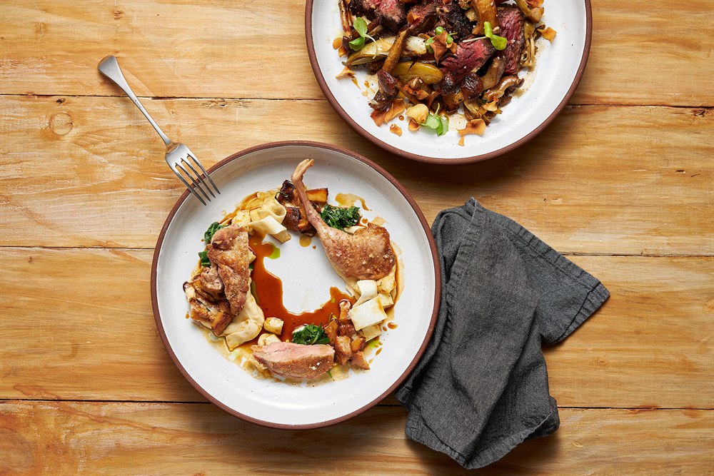Overhead restaurant photography of roast duck with chanterelles and sliced steak with roasted vegetables
